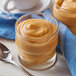 A glass of Cafe Classics Butterscotch Pudding with a spoon on a table with a blue napkin.