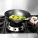 A hand cooking broccoli in a Town mandarin wok on a stove.