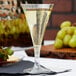 A clear plastic Fineline Tiny Barware champagne flute filled with champagne sits on a table with grapes and strawberries.