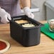 A woman in gloves using a Carlisle Coldmaster divided food pan to prepare food on a counter.