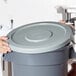 A woman in a lab coat holding a grey Continental Huskee trash can lid.