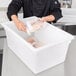 A man holding a bag of chicken in a white Cambro food storage container.