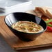 A black slanted melamine bowl filled with hummus on a table.