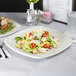 A Tuxton eggshell white china plate with salad on it on a table.