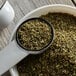 A white measuring cup with a white spoon filled with Regal Marjoram leaves.