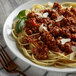 A plate of spaghetti with Regal Marjoram Leaves, meat sauce, and parmesan cheese on a white background with a fork.