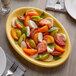 A Tuxton saffron oval china coupe platter with tomatoes, mozzarella, and basil on a table.