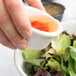 A person pouring liquid from a Thunder Group bone fluted ramekin over a bowl of salad.