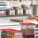 A woman uses a Metro clear plastic label holder on a shelf to label a plastic container of food.