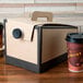 A cardboard box with a lid and two coffee cups on a table.