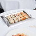 A Vollrath stainless steel serving tray with sushi on a table.