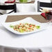 A white Milano melamine square plate with pasta and a drink on a table.