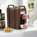 A person pouring coffee into a Cambro dark brown insulated beverage dispenser.