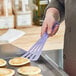 A hand holding a purple Mercer Culinary slotted turner over pancakes.