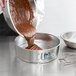 A person pouring brown liquid into a Winco light tin springform cake pan.