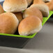 A green and black square melamine bowl filled with bread rolls.