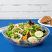 A salad in a Fineline clear plastic bowl with a fork.