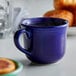 A blue Tuxton round china cup with liquid in it on a table.