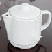 An Arcoroc white porcelain teapot on a table with a tea bag attached.