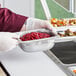 A person in gloves holding a Vollrath stainless steel steam table pan full of food.