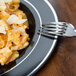 A Fineline black plastic plate with silver bands holding a plate of pasta with a fork.