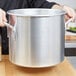 A person holding a large silver Vollrath stock pot.