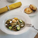 A Tuxton Seabreeze eggshell china plate with a bowl of pasta with vegetables and cheese on it.