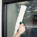 A hand using a Unger ErgoTec T-Bar StripWasher to clean a window.