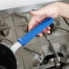 A hand using a Vollrath blue silicone pan handle sleeve to hold a pan over a stove.