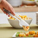 A hand using Carlisle stainless steel pastry tongs to serve food in a bowl.