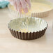 A person sprinkling shredded cheese into a deep tart.