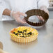 A person holding a Gobel deep fluted tart pan with a quiche in a pastry case with green toppings.