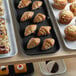 A black Cambro market tray holding pastries and muffins on a bakery display counter.