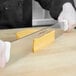 A person using a Dexter-Russell double white handled cheese knife to cut cheese.