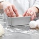 A person's fingers holding dough in a Chicago Metallic bread loaf pan.