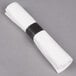 A white linen-feel napkin rolled with a black band.