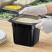A person in gloves holding a black Cambro food container on a counter.