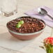 A Sabert clear plastic bowl filled with chocolate pudding with a spoon on a napkin.