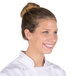 A woman in a white chef's uniform smiling while wearing a brown Royal Paper lightweight hairnet.