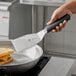 A hand holding a Mercer Culinary heavy duty turner over a pan of food.