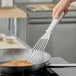 A hand using a Victorinox slotted spatula to cook food in a pan.