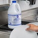 A person holding a white jug with a blue label of Pure Bright Bleach.