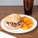 A sandwich on a Dart white foam plate with chips and a drink.