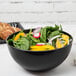 A Fineline black plastic bowl filled with salad and croissants on a table.