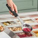 A hand holding a Vollrath black perforated round Spoodle over a bowl of food.