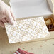A hand holding a white 3-ply paper with a gold floral pattern.