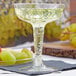 A clear Fineline plastic champagne glass filled with champagne next to green grapes.