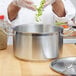 A person using a Vollrath silver sauce pot with a metal lid and handle to cook celery.