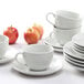 A stack of Tuxton bright white coffee cups and saucers on a white surface.