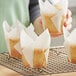 A woman holding a paper bag of Hoffmaster white tulip baking cups with a muffin inside.